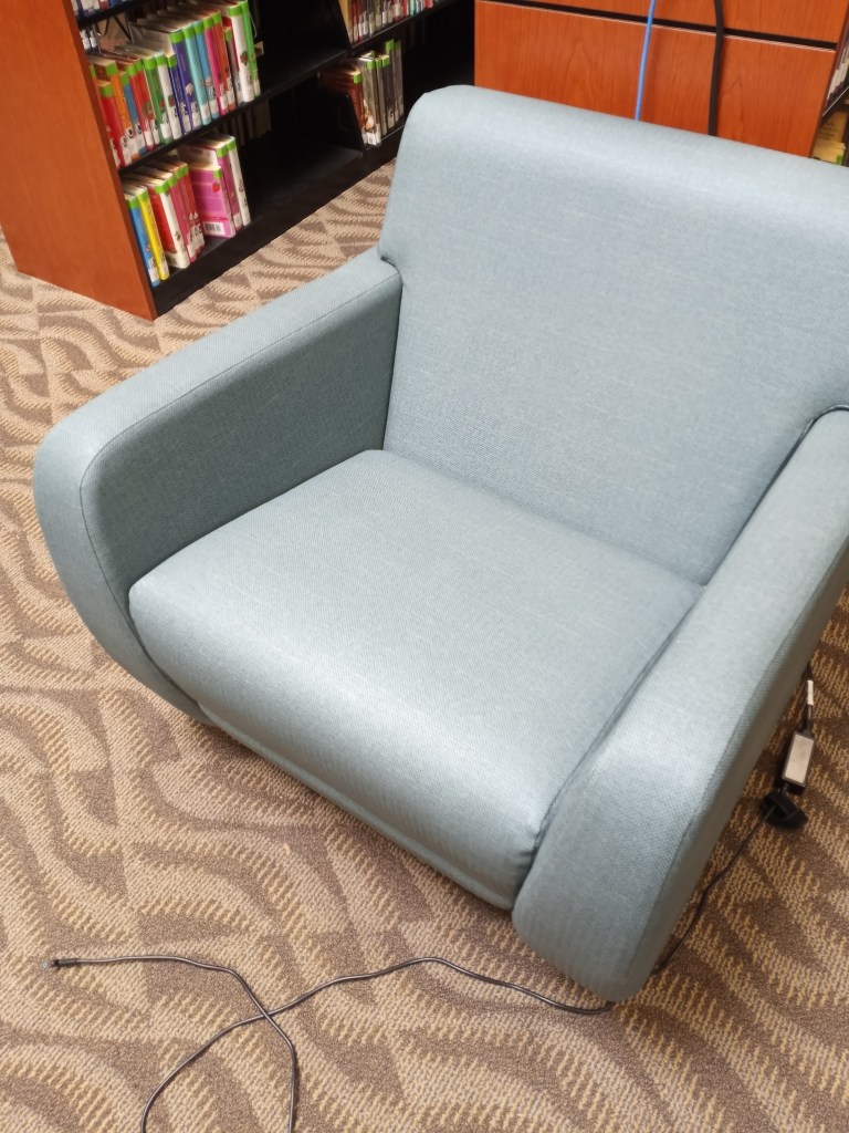 A light blue vinyl armchair is pushed up against the end of a library bookshelf. 