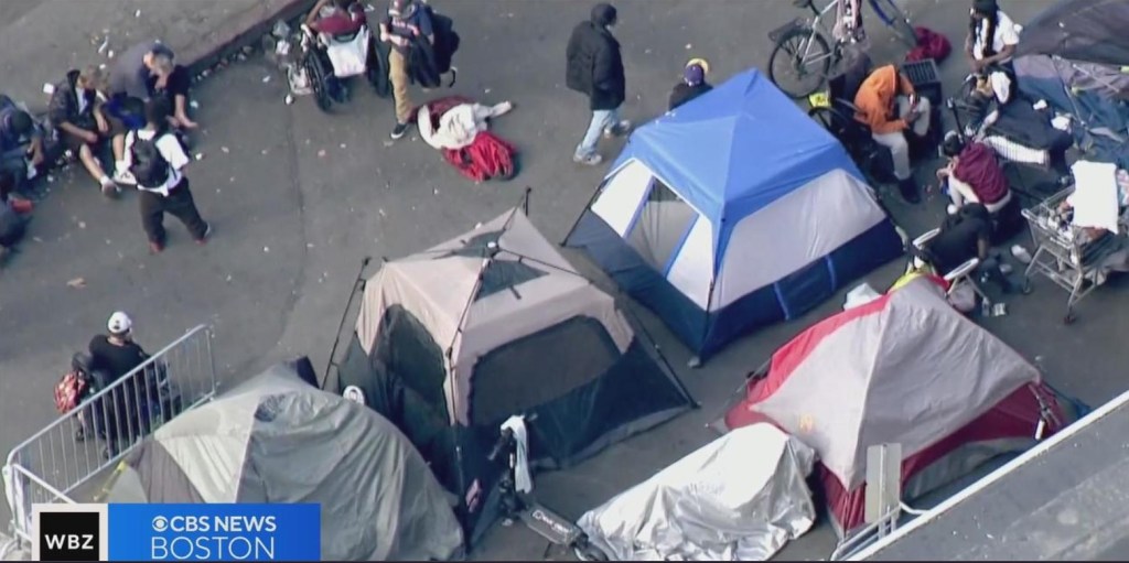 WBZ CBS News Boston arial screenshot of tents belonging to unhoused people at Massachusetts Avenue and Melnea Cass Boulevard in Boston, Massachusetts. 