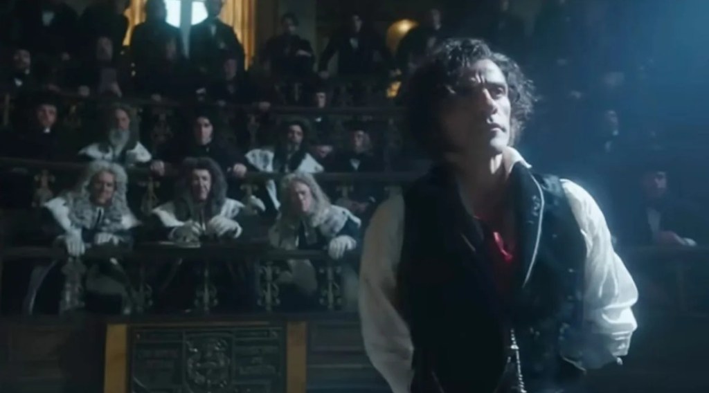 A defiant Victor Frankenstein stands in front of a tribunal of skeptical and concerned medical professionals in old-fashioned white wigs. 