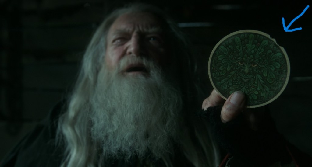 The old man with long white hair and beard holds up a round card. The edge of the card has little bites taken out of it. A blue arrow points to the bites.
